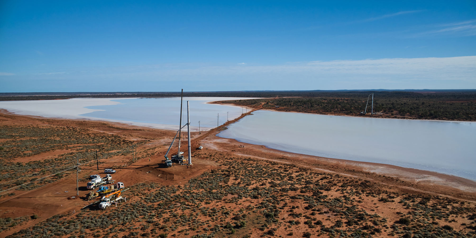 An aerial photo of transmission poles being installed in a rural setting near a body of water.