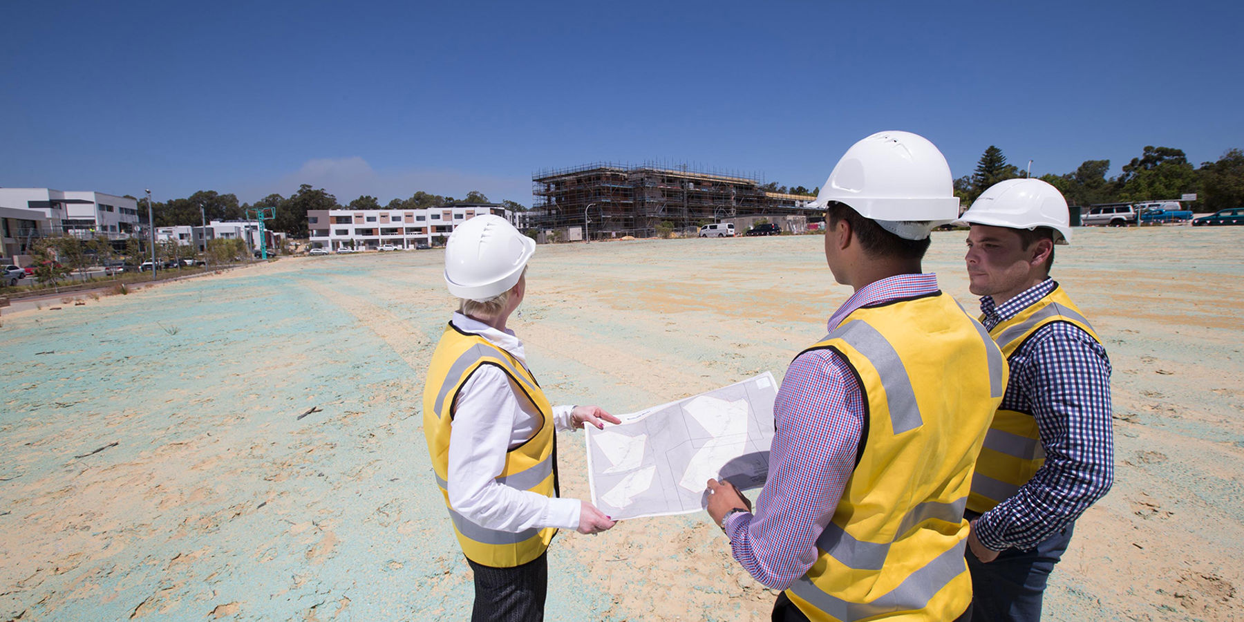 Three people in high-visibility clothing and construction hats looking at plans on a construction site.